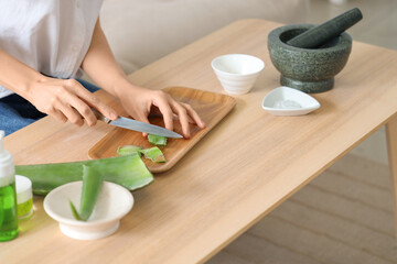 Beautiful young woman cutting aloe vera leaf in living room, closeup