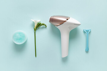 Modern photoepilator with jar of scrub, razor and flower on turquoise background