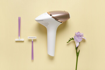 Modern photoepilator with razors and flower on yellow background