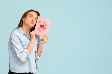 Beautiful young woman holding greeting card with hearts on blue background. Valentine's Day celebration