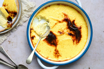 Custard flan in round, enamel dish half eaten with a spoon, landscape