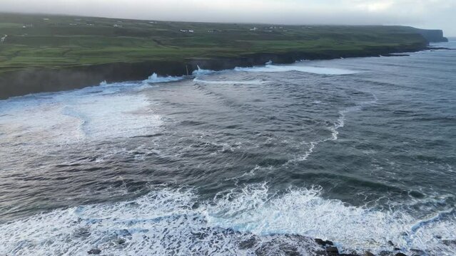 Wwild Atlantic waves crashing against the cliffs of Doolin, Ireland, with lush green fields in the background, aerial view