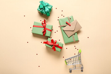 Small shopping cart with gift boxes, envelope and confetti on beige background. Valentine's Day celebration