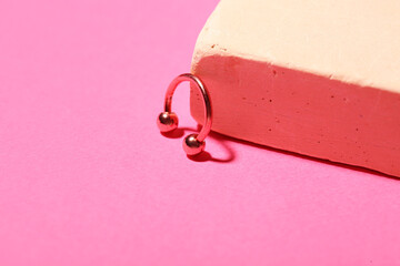 Plaster podium and circular barbell for piercing on pink background