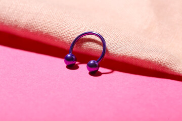 Circular barbell for piercing and cloth on pink background