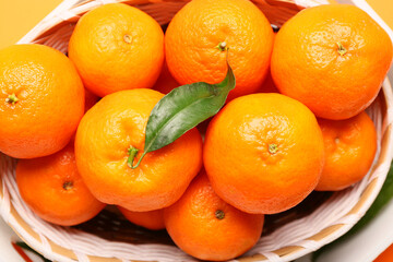 Basket with tasty tangerines and leaf on orange background, closeup