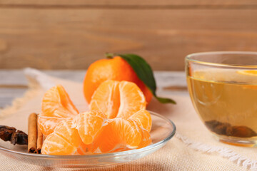 Cup of tea and plate with fresh tangerine segments on wooden background