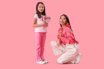 Little Asian girl greeting her mother with Valentine's day on pink background