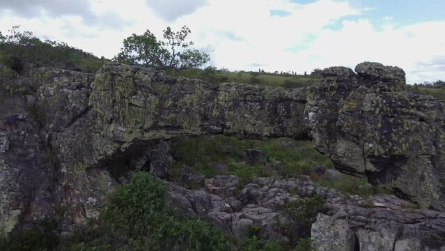 Aerial skims jagged surreal rocky slope up and over natural stone arch