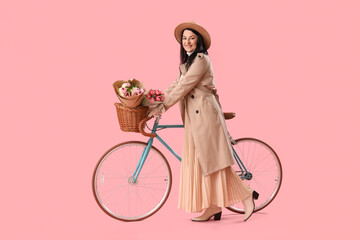 Beautiful stylish happy mature woman with bicycle and bouquet of tulips on pink background....