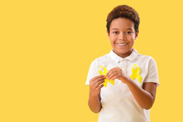 Cute little African-American boy with yellow ribbons on color background. Childhood cancer awareness concept