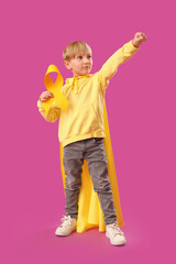 Cute little boy in superhero costume with yellow ribbon on purple background. Childhood cancer awareness concept