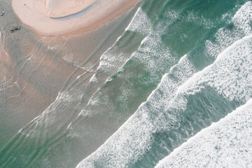 Aerial shot of the foamy waves of the ocean hitting the sandy shore