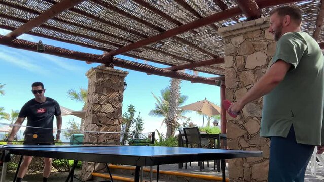 Two guys playing a competitive game of ping pong outside during the day at a hotel or resort