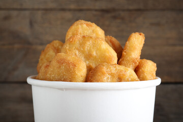 Bucket with tasty chicken nuggets on wooden background, closeup