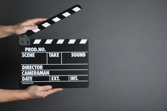 Woman holding clapperboard on dark grey background, closeup with space for text. Cinema production