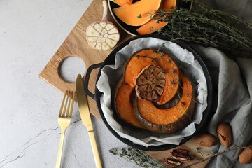 Freshly baked pumpkin slices with garlic and thyme on light table, flat lay