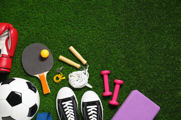 Different sports equipment on green grass, flat lay. Space for text