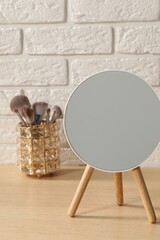 Mirror and makeup brushes on wooden dressing table in room