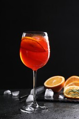 Glass of tasty Aperol spritz cocktail with orange slices and ice cubes on table against black background