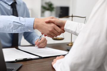 Lawyers shaking hands at wooden table in office, closeup
