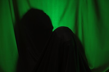 Silhouette of creepy ghost behind dark green cloth