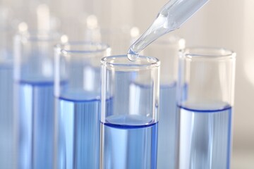 Laboratory analysis. Dripping light blue liquid from pipette into glass test tube on blurred background, closeup