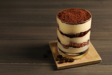 Delicious tiramisu in glass and coffee beans on wooden table, closeup. Space for text
