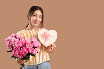 Beautiful young Asian woman with bouquet of pink chrysanthemum flowers and gift box on brown background. International Women's Day