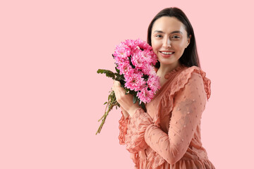 Happy young woman with bouquet of pink chrysanthemum flowers on color background. International...