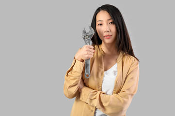 Young Asian woman with adjustable wrench on grey background. Women history month