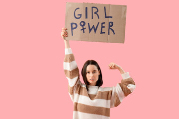 Beautiful young woman holding paper with text GIRL POWER and showing muscles on pink background....