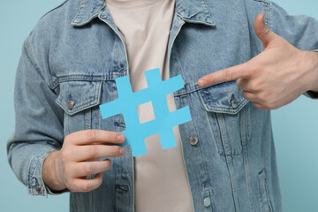 Man pointing at hashtag sign on blue background, closeup