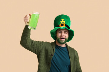 Happy young man in leprechaun hat with green beard holding glass of beer on beige background. St....