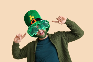 Young man in leprechaun hat and decorative glasses in shape of clover with green beard on beige...