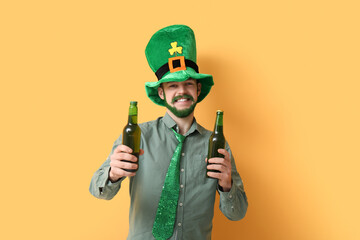 Young man in leprechaun hat with green beard holding bottles of beer on yellow background. St....