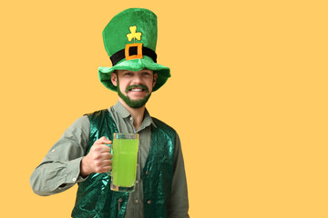 Happy young man in leprechaun hat with green beard holding glass of beer on yellow background. St....