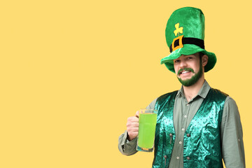 Happy young man in leprechaun hat with green beard holding glass of beer on yellow background. St....