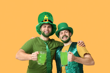 Happy young men in leprechaun hats with green beards holding glasses of beer on yellow background....
