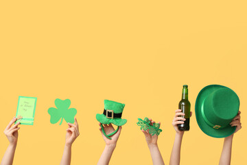 Female hands holding beer and party decor for St. Patrick's Day celebration on yellow background