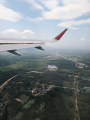 A view from an airplane window during flight, capturing part of the plane’s wing and the landscape below. The airplane’s wing is grey with a red-tipped winglet.