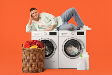 Handsome young man lying on washing machines against orange background