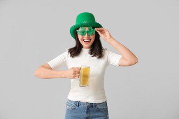 Beautiful young woman in leprechaun hat and decorative glasses in shape of clover with glass of...