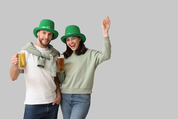 Beautiful young couple in leprechaun hats with glasses of beer on grey background. St. Patrick's...