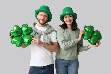 Beautiful young couple in leprechaun hats with air balloons in shape of clover on grey background....
