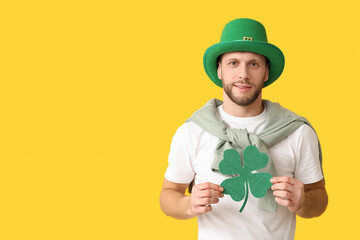 Young man in leprechaun hat with clover on yellow background. St. Patrick's Day celebration