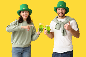 Beautiful young couple in leprechaun hats pointing at glasses of beer and showing thumb-up gesture...