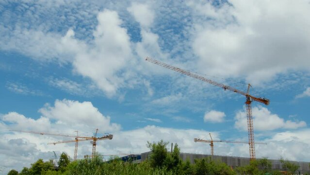 Timelapse of cranes working on building construction and moving clouds and blue sky. Timelapse of skyscraper building construction with cranes on the roof. Construction Timelapse.