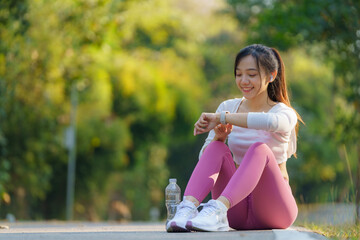 Healthy women relax after cooling down and looking for smartwatches to check timing runs. Asian runner woman workout after fitness and jogging session at the park. Healthy and lifestyle concept.