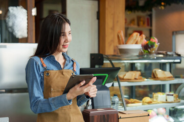 Beautiful Asian barista holds a tablet showing customers a menu and smiles in front of the counter....